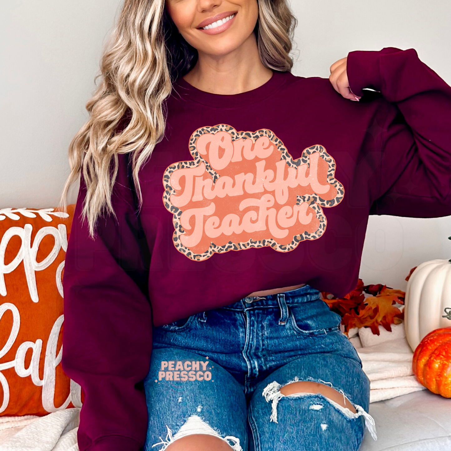 Woman wearing a maroon crewneck sweatshirt featuring a retro One Thankful Teacher design with a leopard print border, ideal for autumn teachers.
