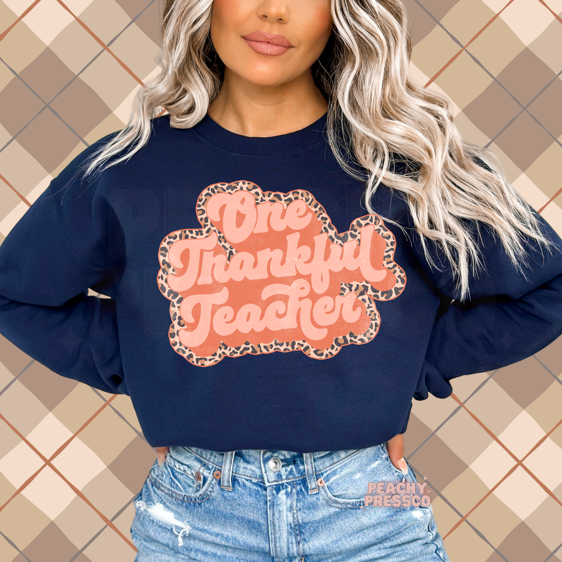 Woman wearing a navy crewneck sweatshirt featuring a retro One Thankful Teacher graphic with a leopard print outline for Thanksgiving and fall.