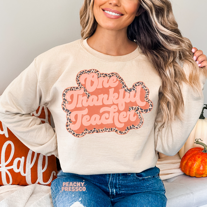 Woman wearing a sand crewneck sweatshirt featuring a retro One Thankful Teacher graphic with a trendy leopard print outline, perfect for fall and Thanksgiving.