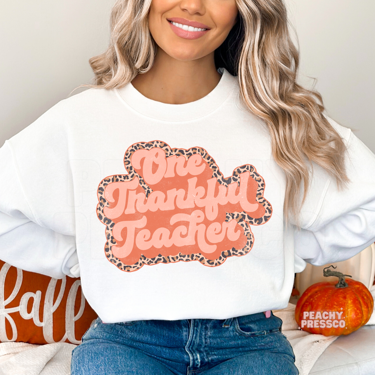 Woman wearing a white crewneck sweatshirt featuring a retro One Thankful Teacher graphic with a leopard print outline, perfect for teachers during fall.