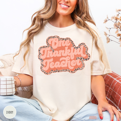 Woman wearing an ivory graphic t-shirt featuring a retro One Thankful Teacher design with a leopard print outline for fall.