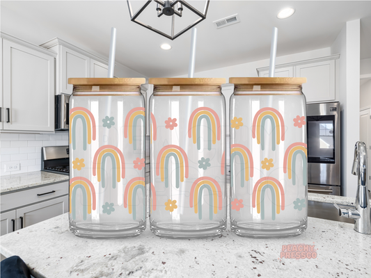 16 oz glass cup featuring a repeating pattern of pastel rainbows and small retro flowers with a bamboo lid and reusable glass straw.