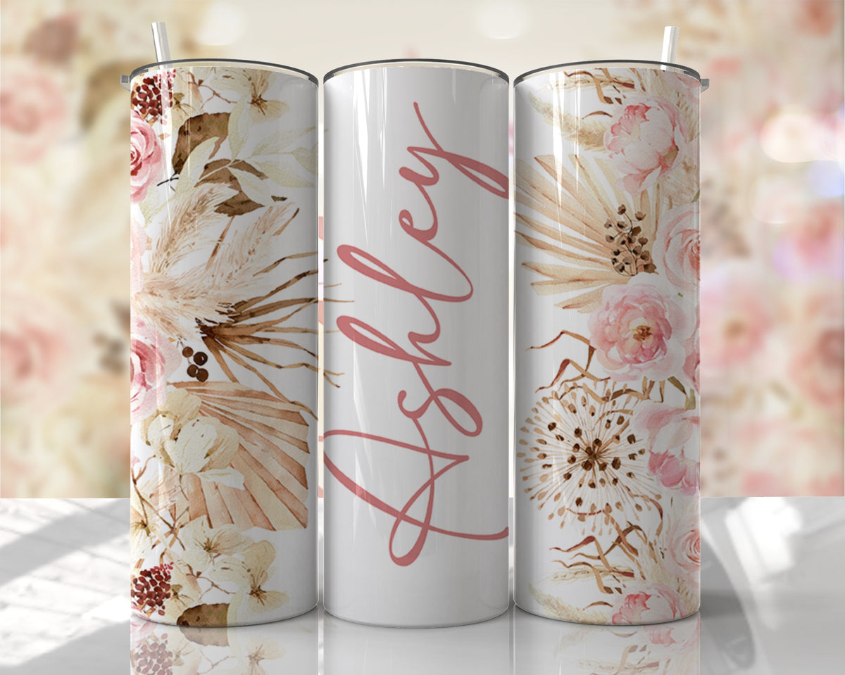Personalized 20 oz skinny tumbler with blush florals, pampas grass, and custom script name on a white background. Includes clear lid and reusable straw.