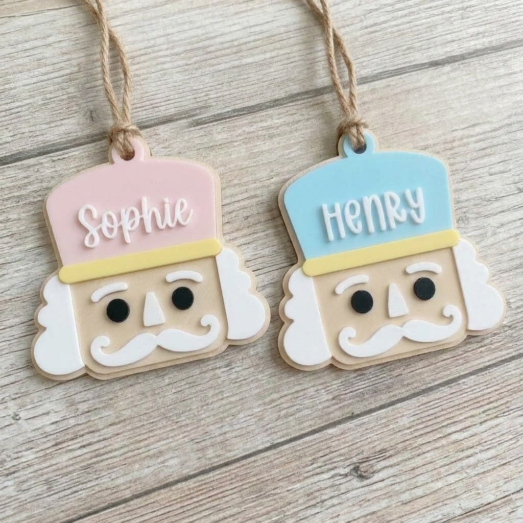 Two custom personalized Nutcracker soldier Christmas ornaments in pink and blue with the names Sophie and Henry, hanging on a wood background