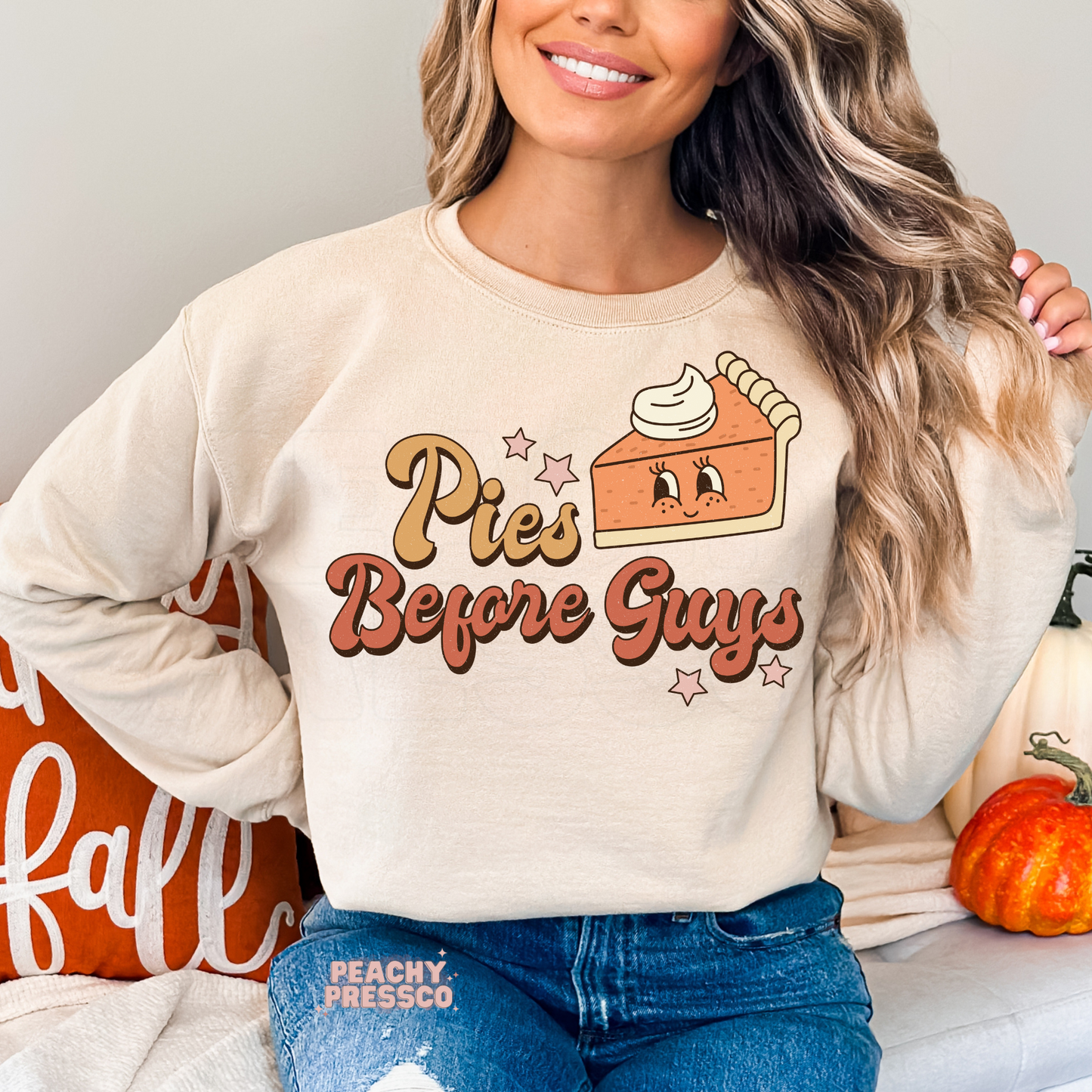 Woman wearing a sand crewneck sweatshirt with a retro "Pies Before Guys" pumpkin pie graphic in warm autumn colors.