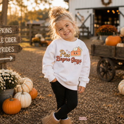 Smiling toddler girl wearing a white "Pies Before Guys" sweatshirt at a pumpkin patch with pumpkins, fall décor, and cozy autumn scenery.