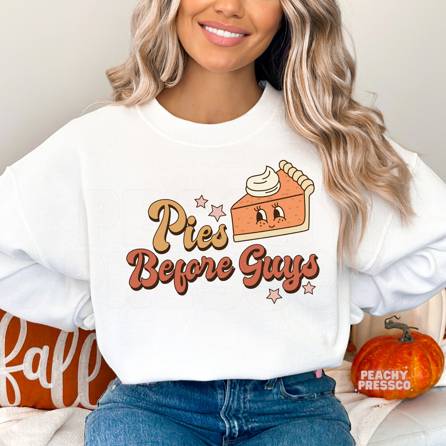 Woman wearing a white crewneck sweatshirt featuring a playful "Pies Before Guys" graphic with a smiling pumpkin pie illustration.