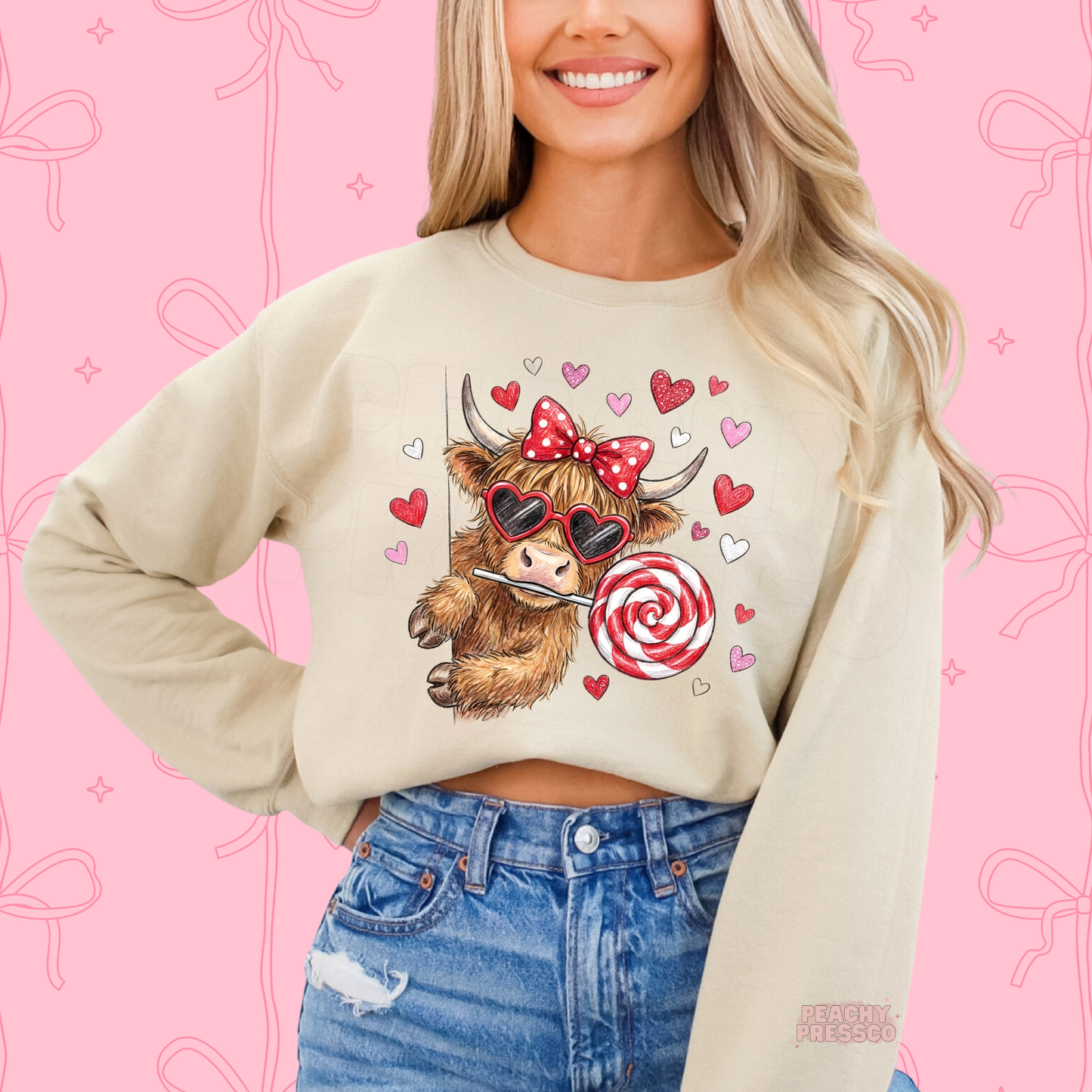Sand sweatshirt displaying a sweet cow wearing heart-shaped sunglasses and a coquette bow while holding a red and white candy lollipop.