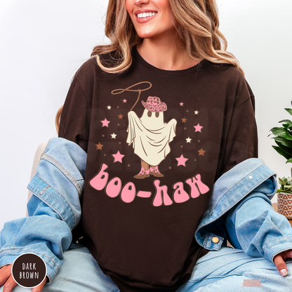 A woman wearing a dark brown graphic t-shirt with a cartoon ghost wearing a pink hat and the text 'boo-haa' in pink, styled with a light blue denim jacket draped off her shoulders.