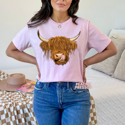 Woman wearing a light pink t-shirt featuring a Highland cow graphic with shaggy hair and a playful expression, perfect for country girls.