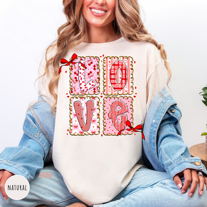 Natural graphic t-shirt displaying a pink patchwork LOVE design with plaid, hearts, cherries, bows, and coquette-inspired Valentine's artwork.