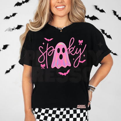 Woman wearing a black t-shirt featuring a cute pink spooky ghost graphic with holographic ghost, bows and bats for Halloween.