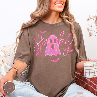 Woman wearing a Comfort Colors Espresso t-shirt featuring a cute pink spooky ghost graphic with holographic ghost, bows and bats for Halloween.