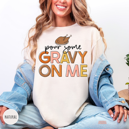 Woman wearing a natural t-shirt featuring a trendy "Pour Some Gravy On Me" Thanksgiving graphic with a roasted turkey and vintage-inspired lettering.