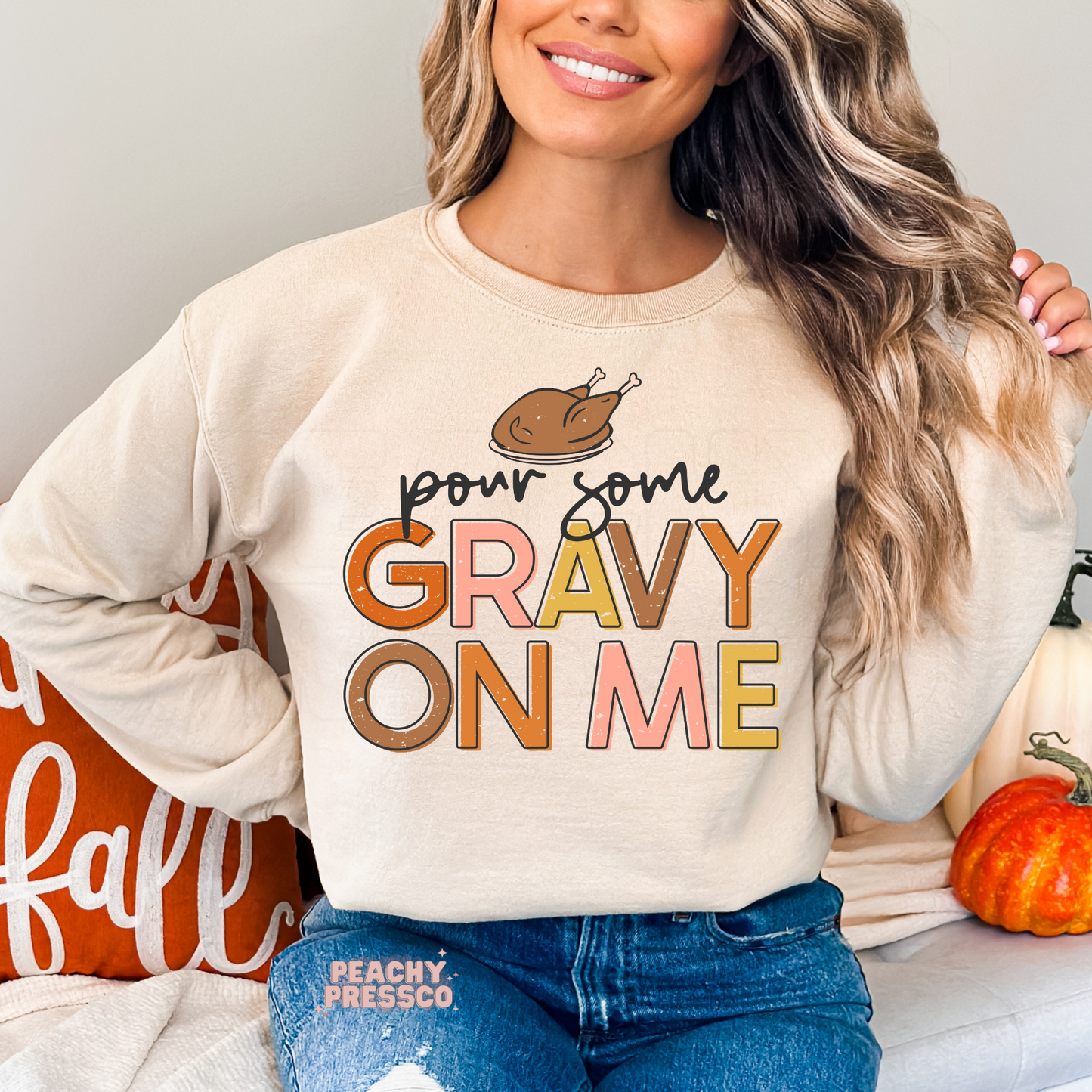 Woman wearing a sand crewneck sweatshirt featuring a funny "Pour Some Gravy On Me" Thanksgiving graphic with a roasted turkey and retro fall lettering.