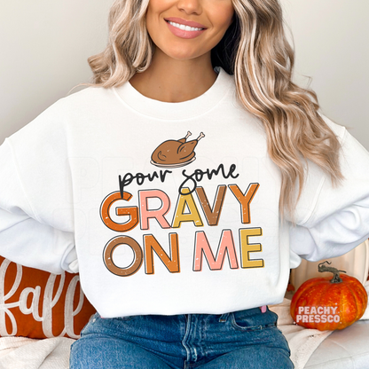 Woman wearing a white crewneck sweatshirt featuring a cute "Pour Some Gravy On Me" Thanksgiving design with a roasted turkey illustration.