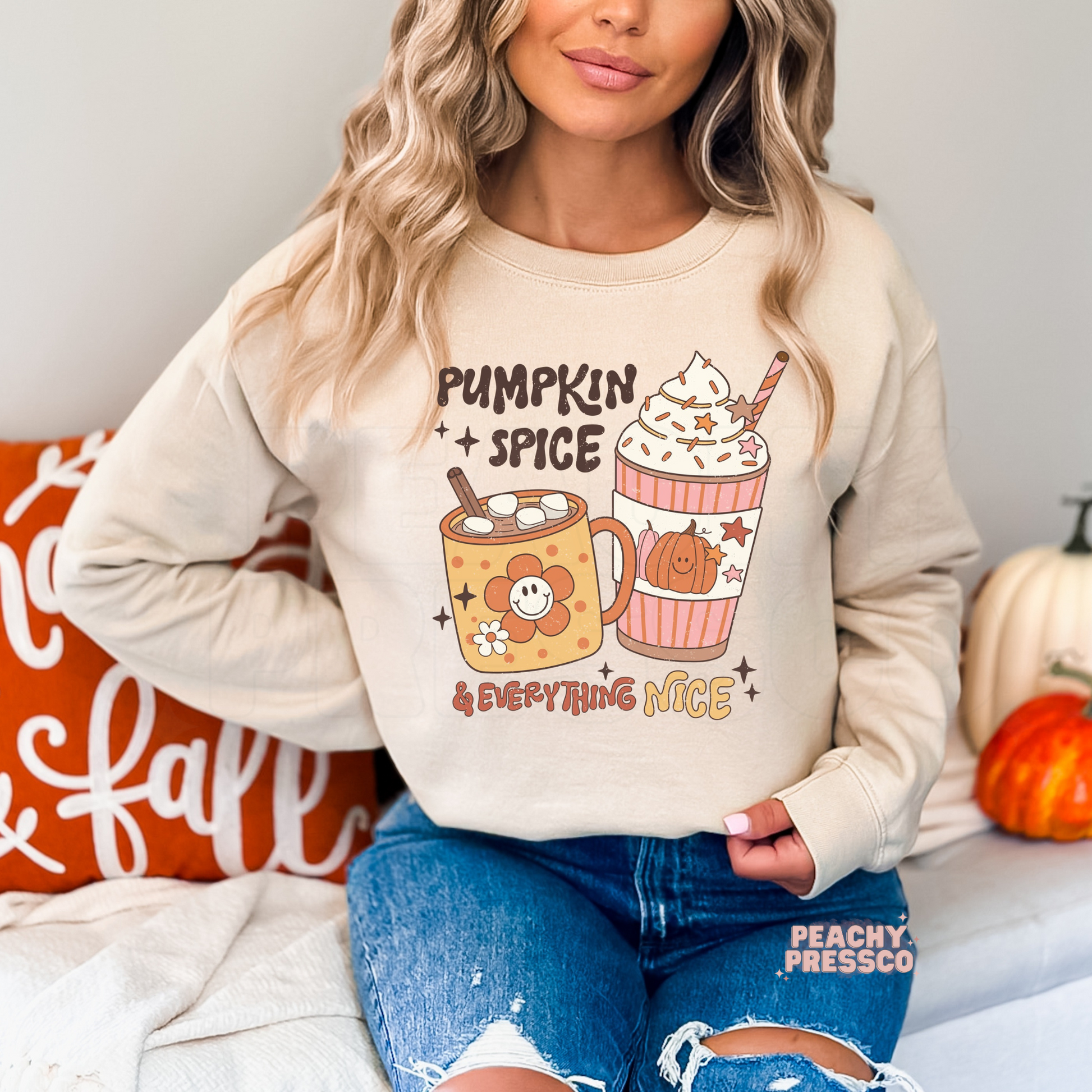 Woman wearing a sand crewneck sweatshirt featuring a cute "Pumpkin Spice & Everything Nice" graphic with a pumpkin spice latte, smiling mug, and cozy fall coffee illustration.