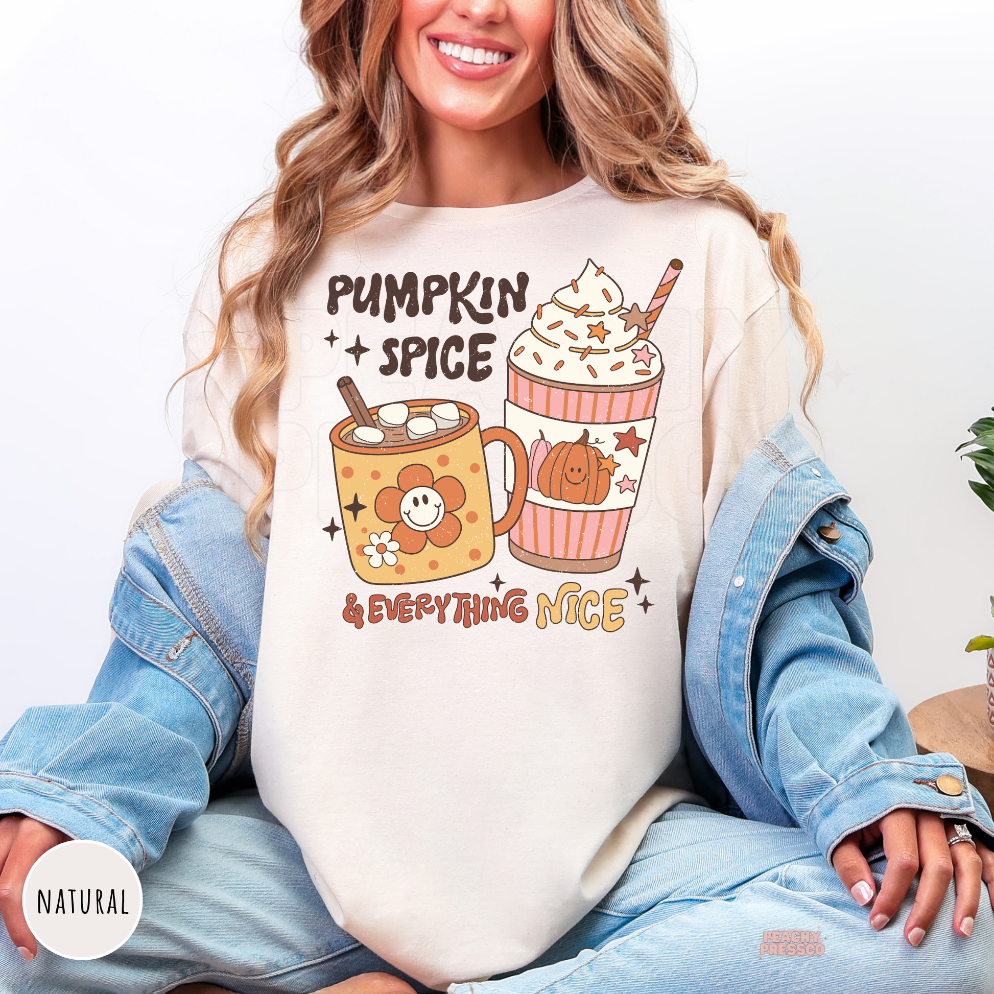 Woman wearing a natural graphic t-shirt featuring a "Pumpkin Spice & Everything Nice" design with a fall latte, hot chocolate mug, pumpkin, and cozy autumn coffee theme.