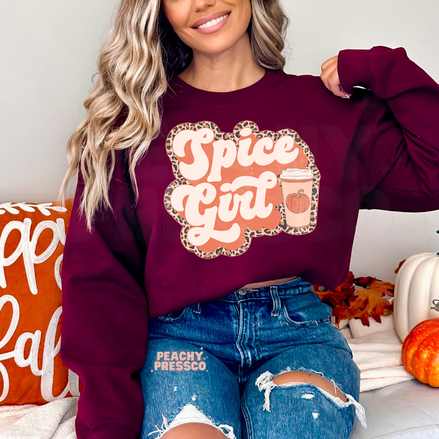 Woman wearing a maroon crewneck sweatshirt featuring a Pumpkin Spiced Girl graphic with a pumpkin coffee cup and leopard print fall design.