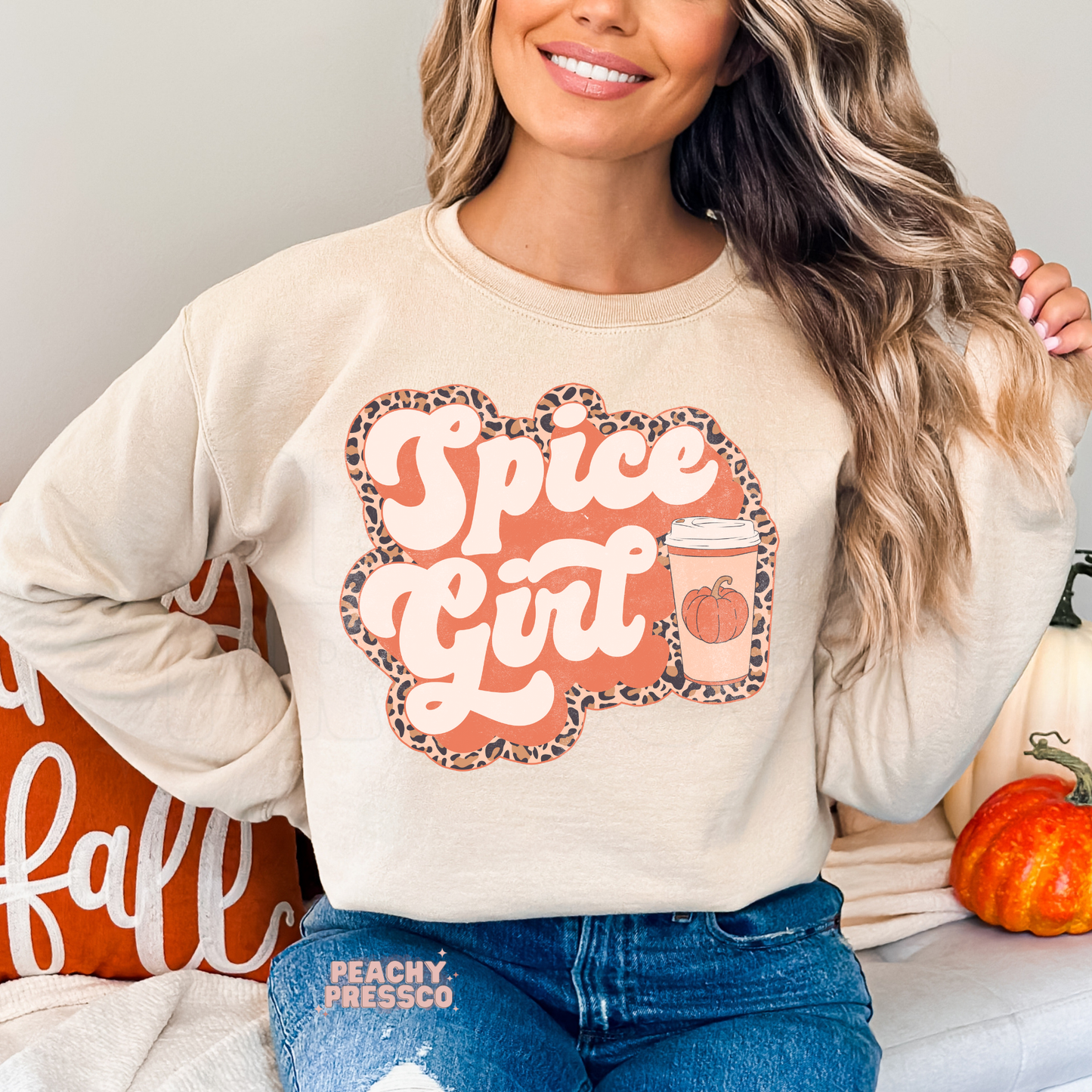 Woman wearing a sand crewneck sweatshirt featuring a Pumpkin Spiced Girl graphic with a pumpkin coffee cup and leopard print accents.