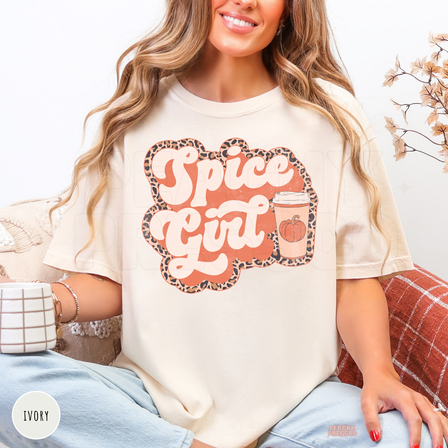 Woman wearing an ivory graphic t-shirt featuring a Pumpkin Spiced Girl design with a pumpkin coffee cup and leopard print border.