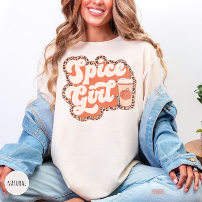 Woman wearing a natural graphic t-shirt featuring a Pumpkin Spiced Girl fall design with a pumpkin coffee cup and leopard print.