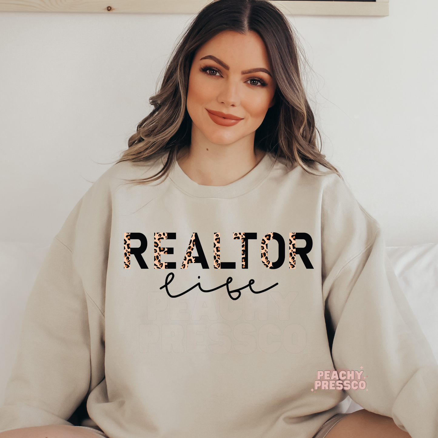 Woman wearing a sand-colored sweatshirt featuring a Realtor Life leopard print design, perfect for real estate agents and closing day celebrations.