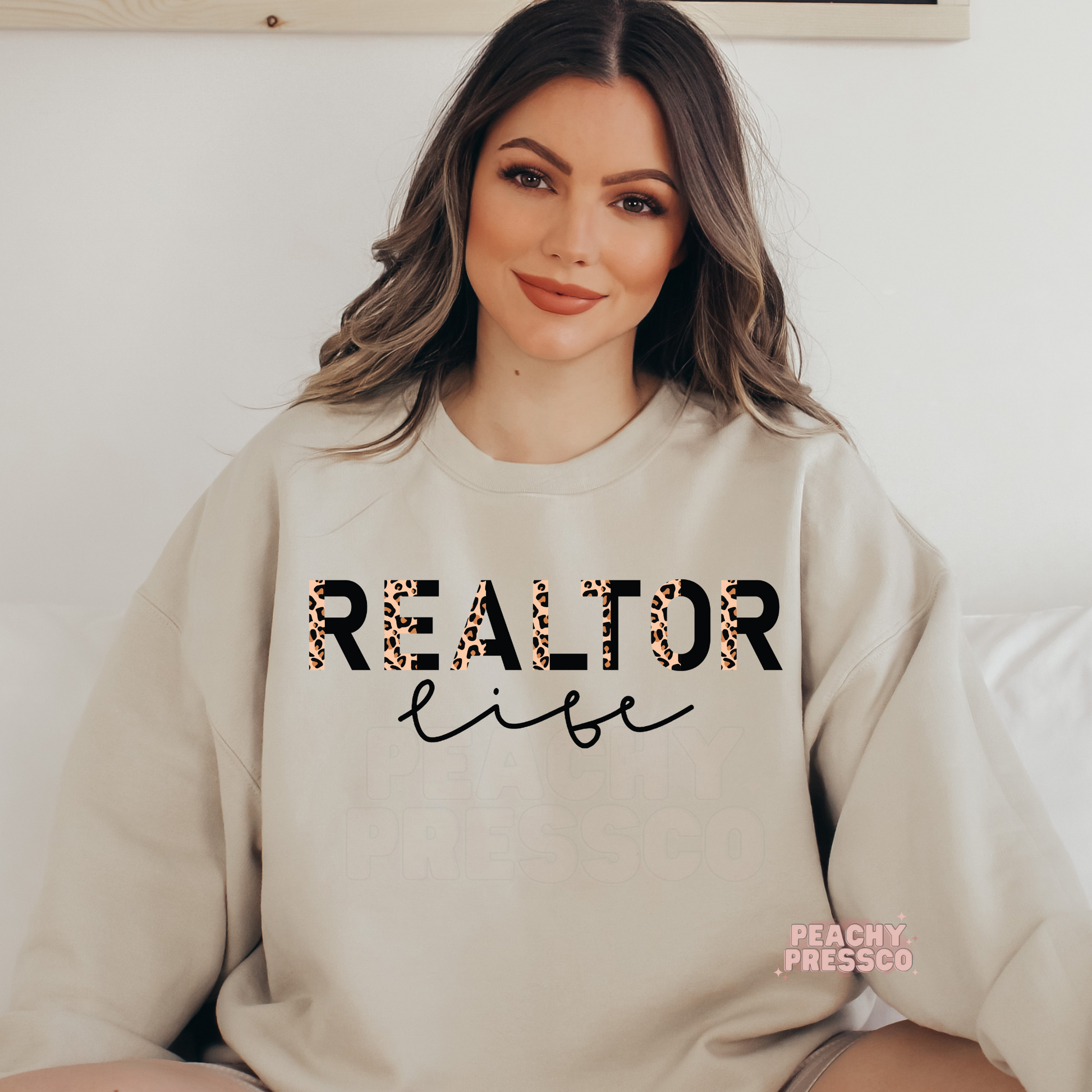 Woman wearing a sand-colored sweatshirt featuring a Realtor Life leopard print design, perfect for real estate agents and closing day celebrations.