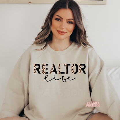 Woman wearing a sand-colored sweatshirt featuring a Realtor Life leopard print design, perfect for real estate agents and closing day celebrations.