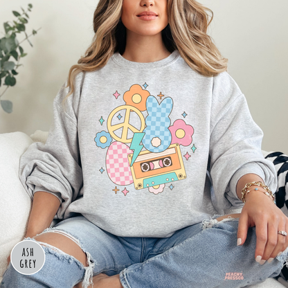Woman wearing an ash grey crewneck sweatshirt with a retro Easter bunny design featuring a cassette tape, pastel flowers, peace sign, and lightning bolt.