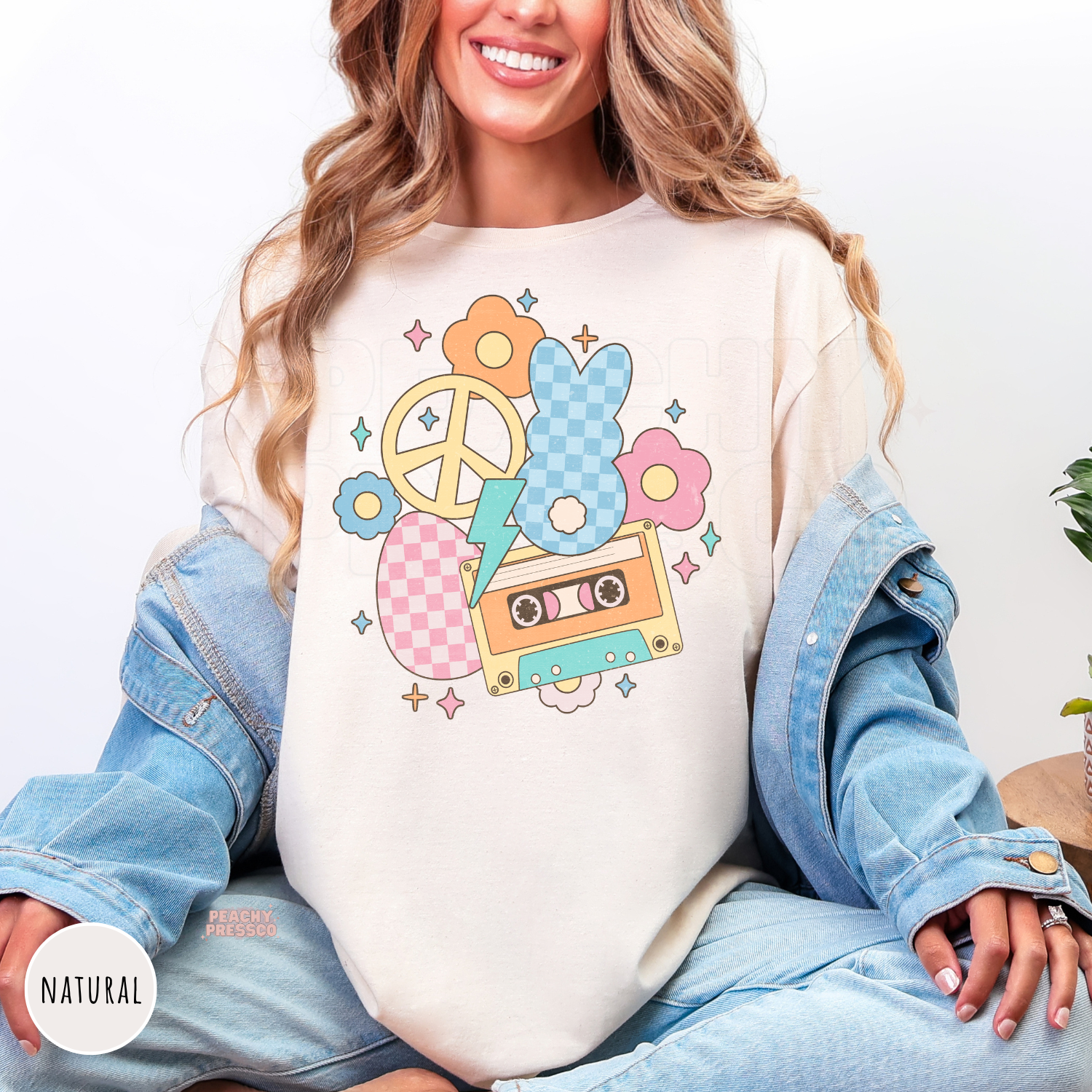 Woman wearing a natural shirt featuring a vintage pastel Easter bunny design with a cassette tape, flowers, peace sign, and lightning bolt.