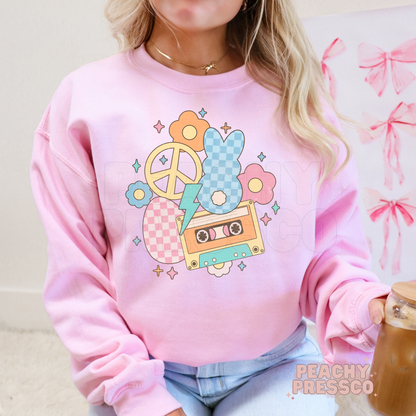 Woman wearing a light pink crewneck sweatshirt featuring a colorful retro Easter bunny design with a cassette tape, flowers, and pastel spring accents.