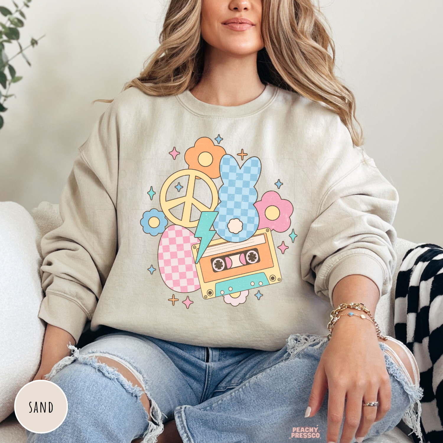 Woman wearing a sand crewneck sweatshirt featuring a vintage pastel Easter bunny graphic with a cassette tape, flowers, peace sign, and lightning bolt.
