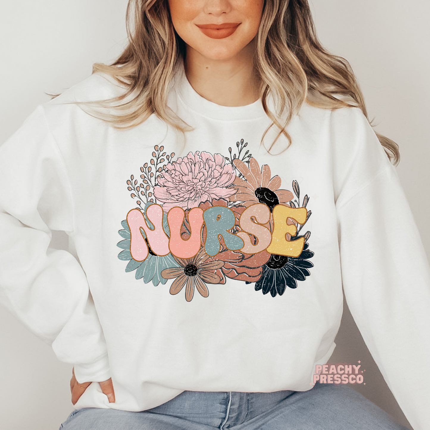 Women wearing a white retro floral nurse sweatshirt with colorful retro "NURSE" graphic surrounded by pastel flowers.
