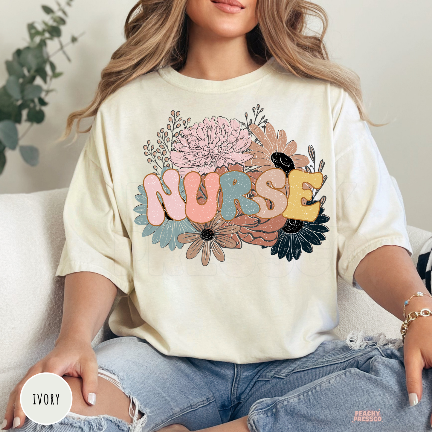 Woman wearing an ivory retro floral nurse t-shirt featuring pastel flowers and colorful nurse lettering.