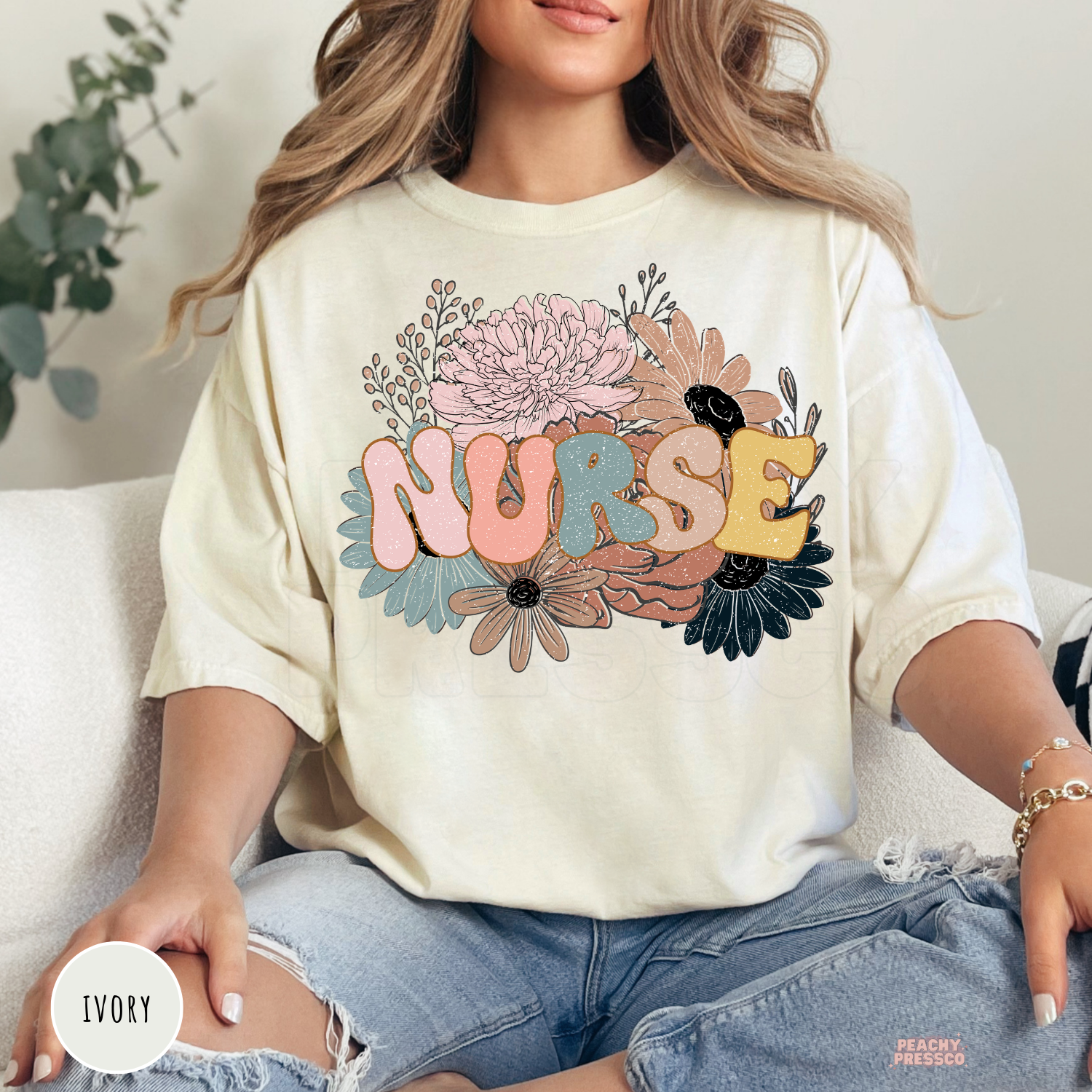 Woman wearing an ivory retro floral nurse t-shirt featuring pastel flowers and colorful nurse lettering.