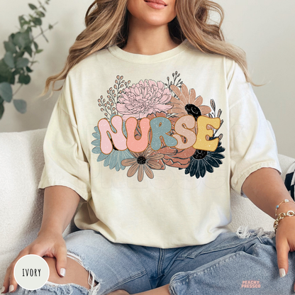 Woman wearing an ivory retro floral nurse t-shirt featuring pastel flowers and colorful nurse lettering.