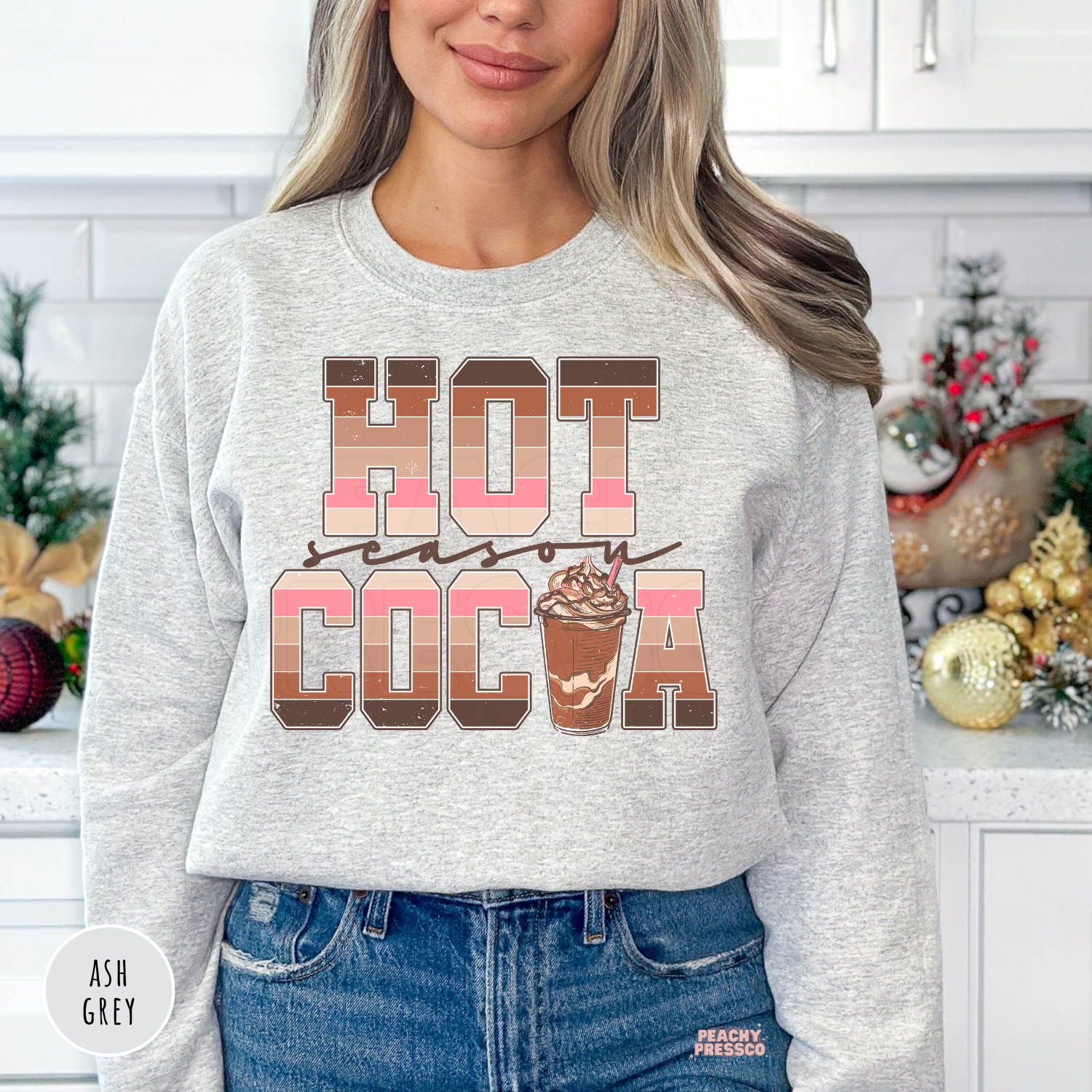 Woman wearing an ash grey Hot Cocoa Season sweatshirt featuring retro striped lettering and a hot chocolate cup graphic.