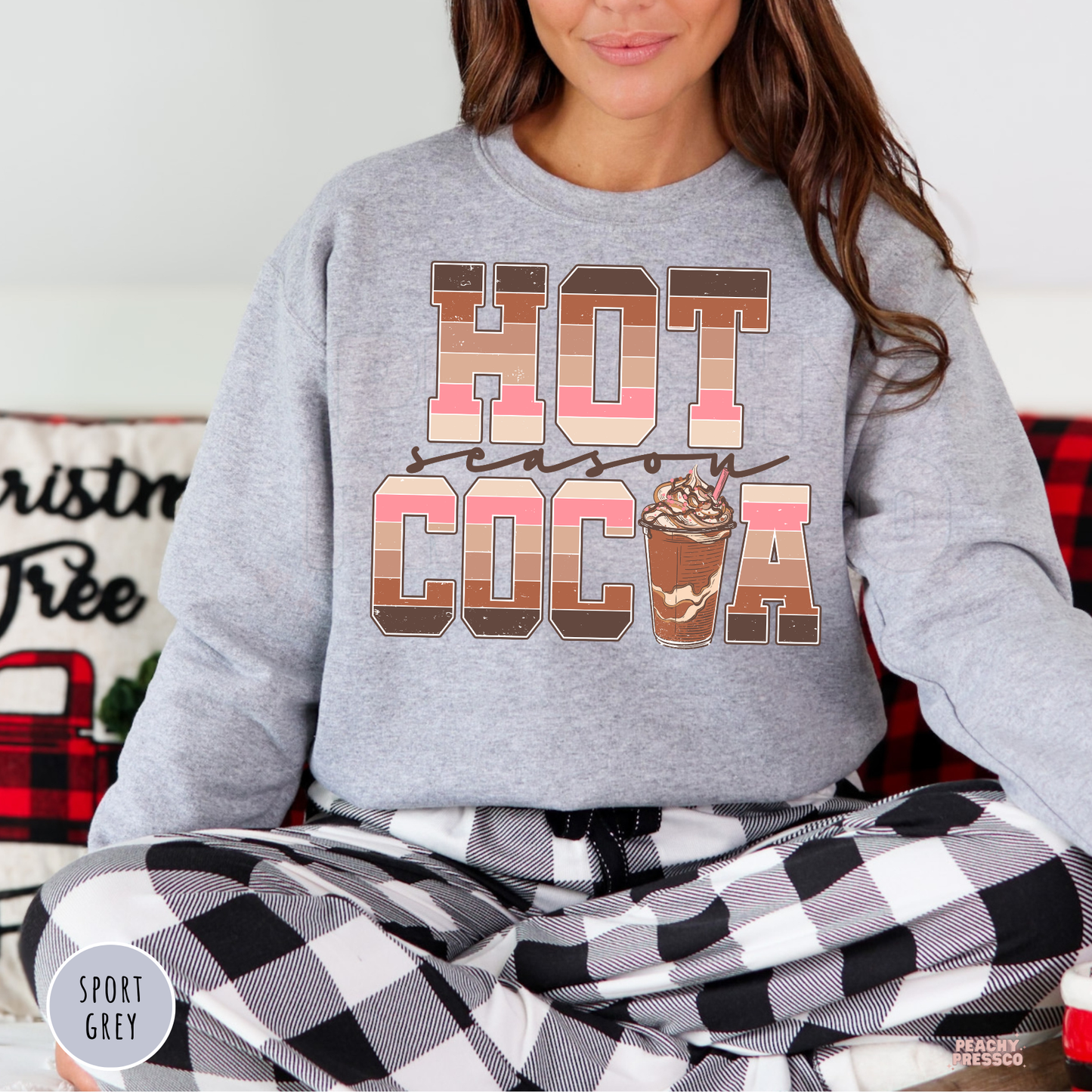 Women wearing a sport grey Hot Cocoa Season sweatshirt paired with black and white buffalo plaid pajama bottoms.