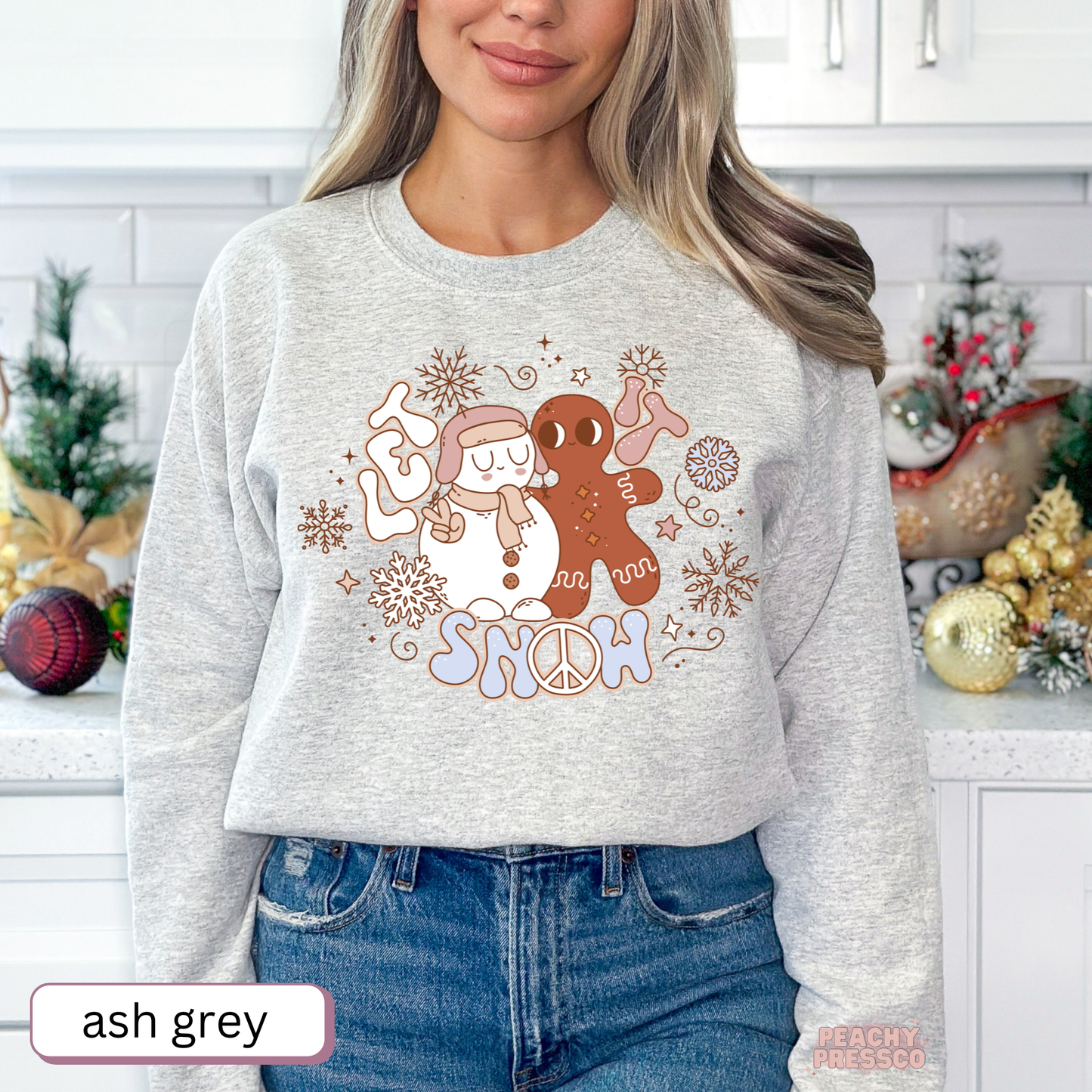 Woman wearing an ash grey Let It Snow holiday sweatshirt with retro snowman, gingerbread, and snowflake artwork.