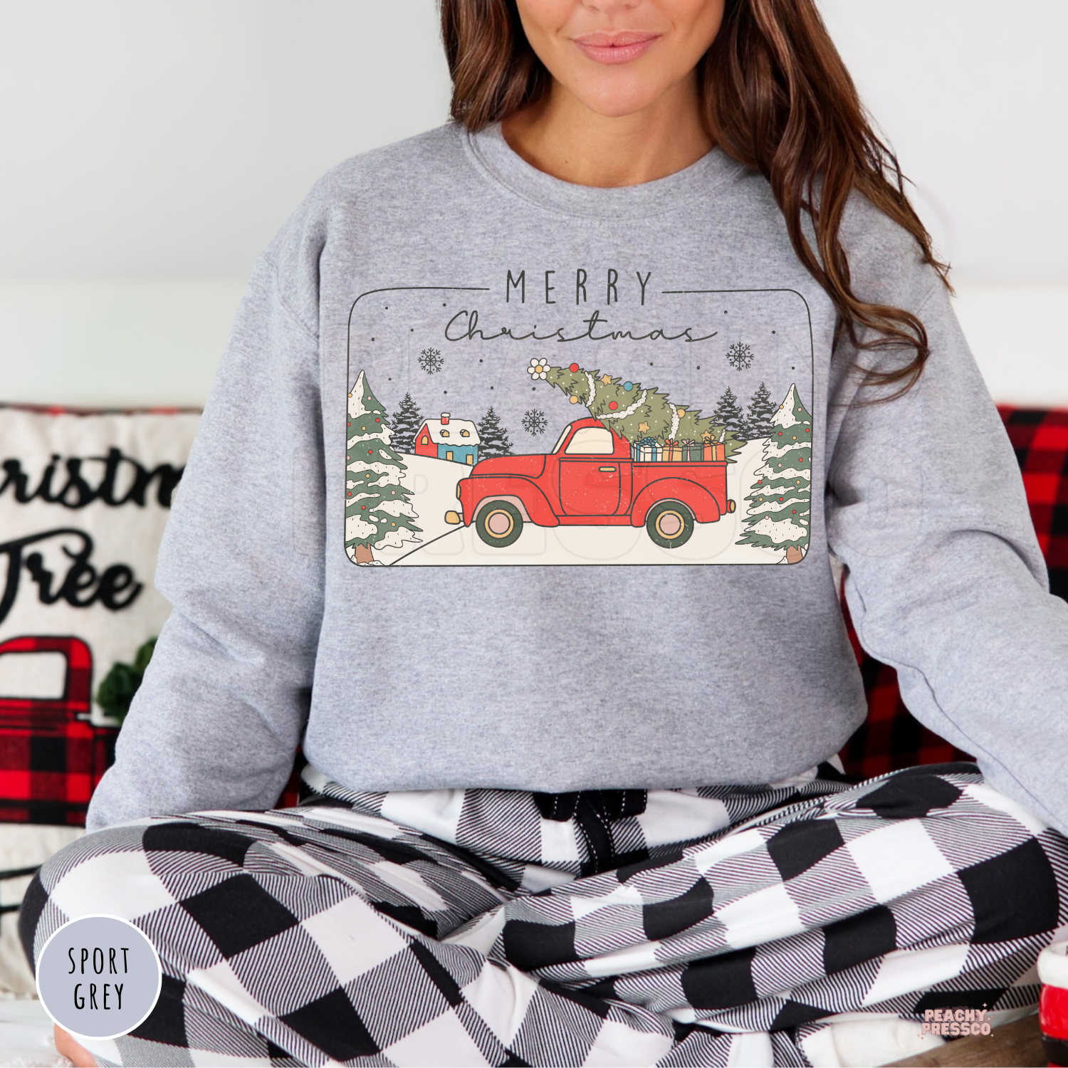 Women sitting cross-legged wearing a sport grey sweatshirt with a retro red Christmas pickup truck design.