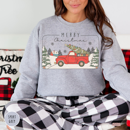 Women sitting cross-legged wearing a sport grey sweatshirt with a retro red Christmas pickup truck design.
