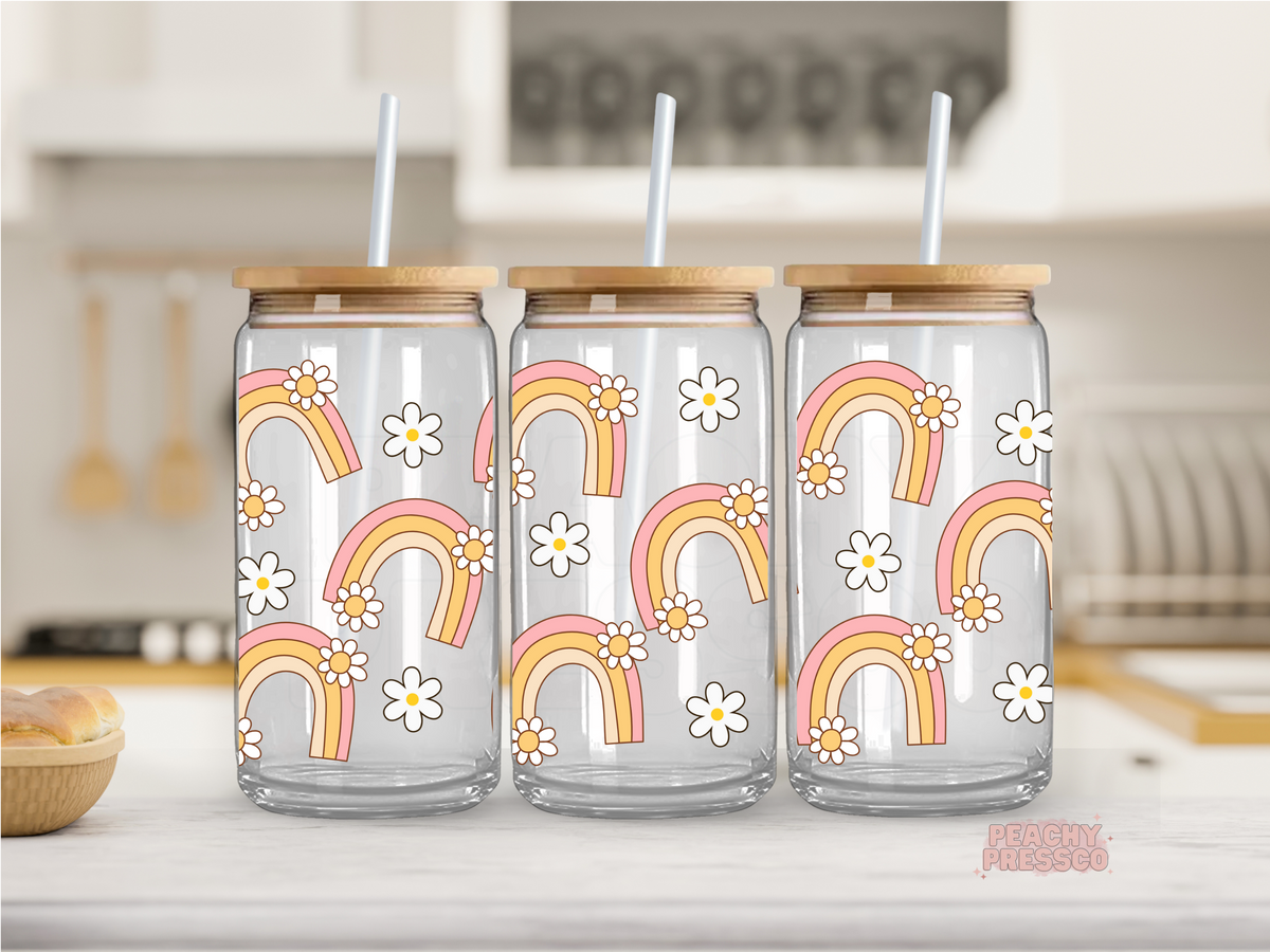 16 oz clear glass cup featuring retro rainbows and white daisy flowers in pink and mustard tones. Includes bamboo lid and reusable straw.