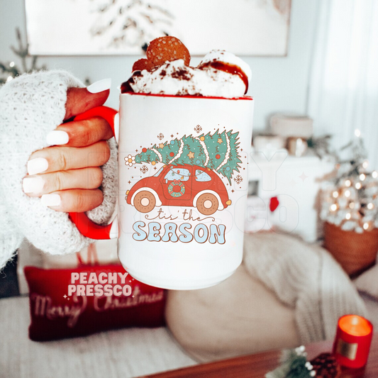 White ceramic mug with red handle and retro red car carrying a Christmas tree on top and groovy text reading tis the Season.