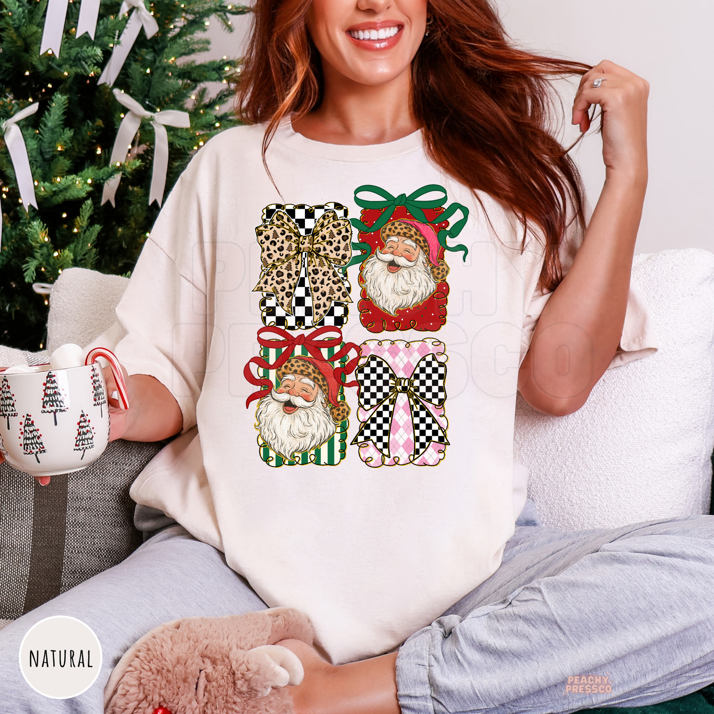 Women relaxing on a couch wearing a natural cream oversized holiday t-shirt featuring leopard bows and retro Santa graphics while holding a mug.