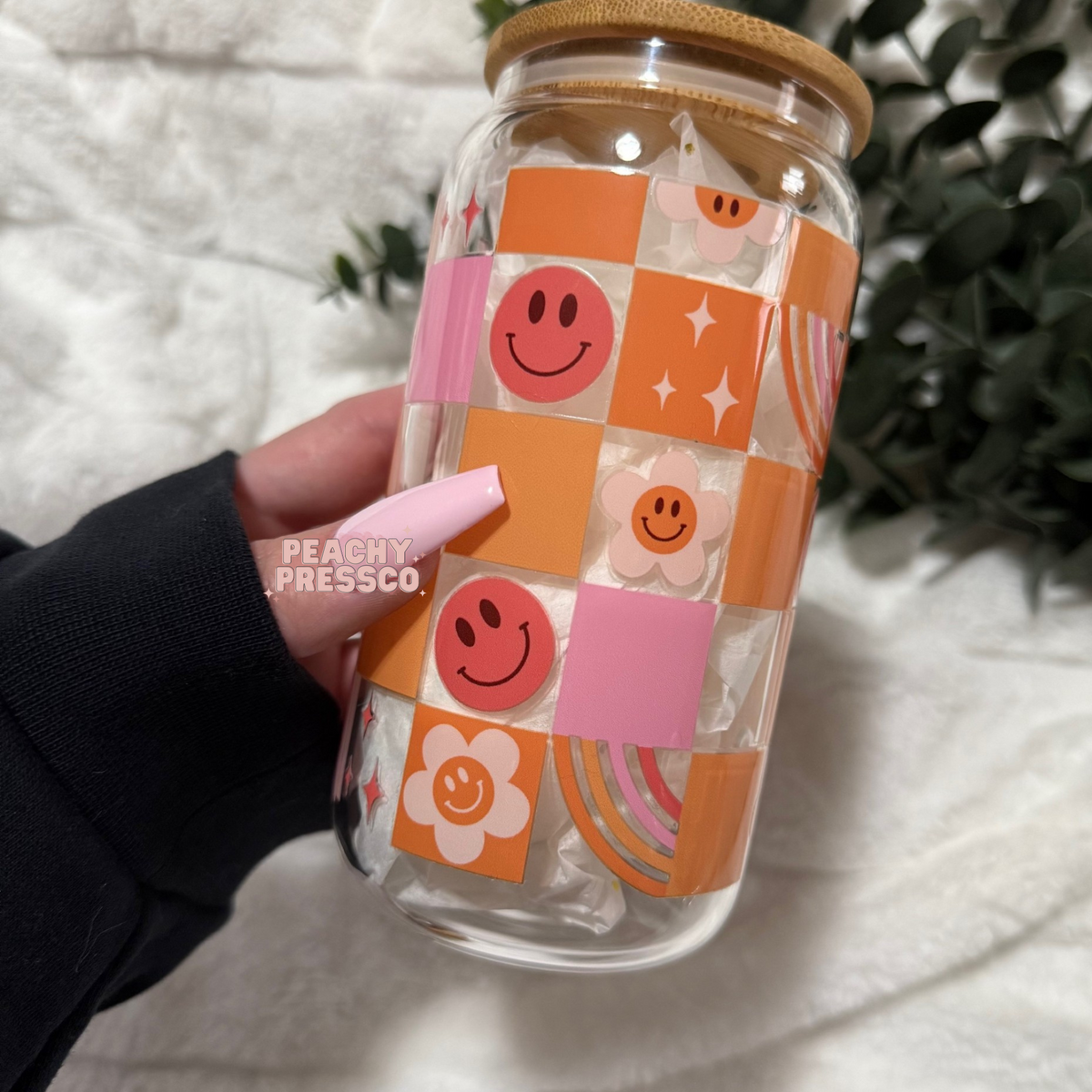 16 oz glass cup featuring a retro patchwork design with smiley faces, flowers, rainbows, and sparkles in soft pastel colors. Includes bamboo lid and reusable straw.