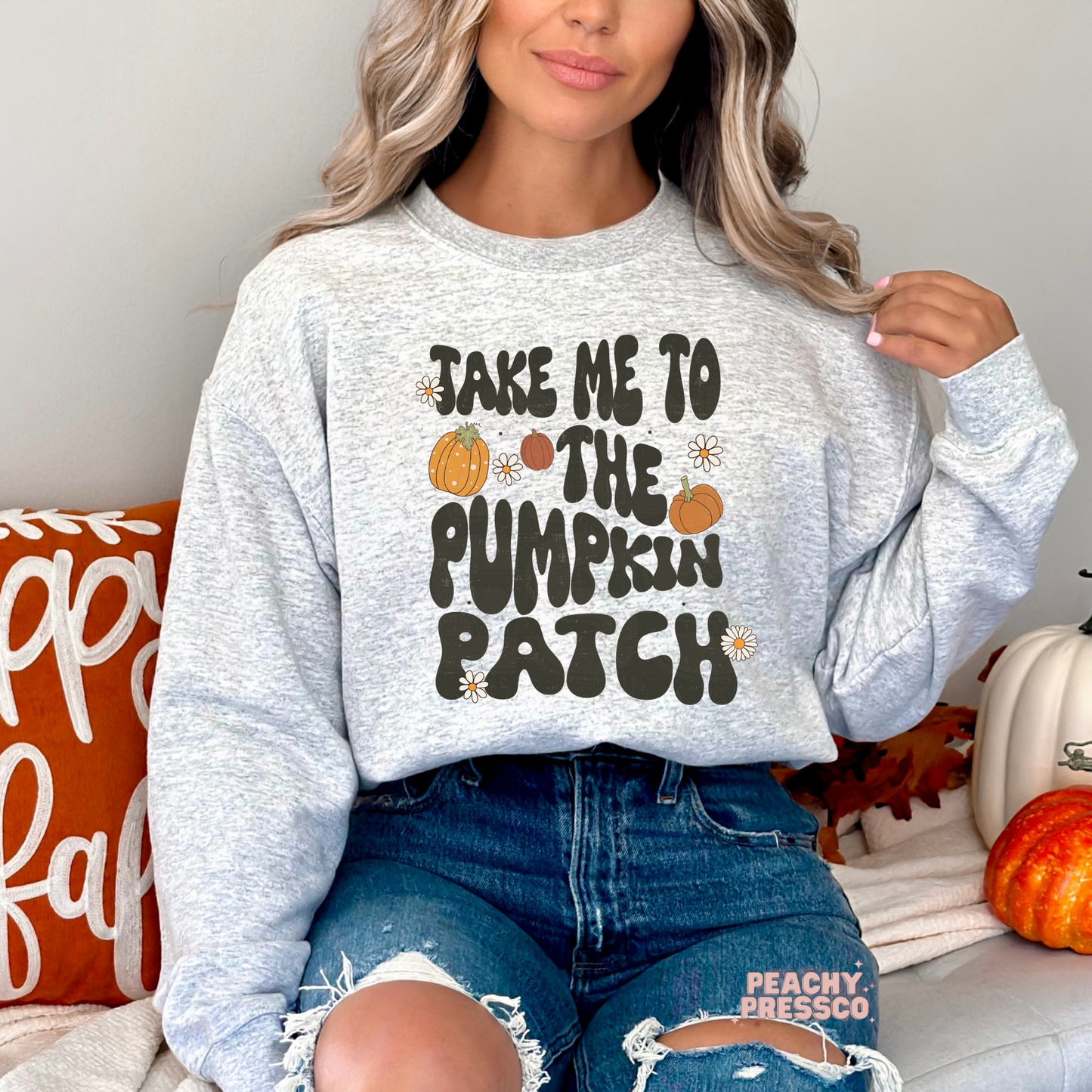 Woman wearing an ash grey crewneck sweatshirt featuring a retro pumpkin patch graphic with pumpkins and daisy accents.