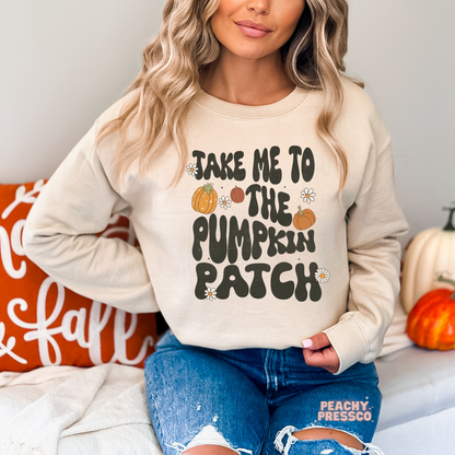 Woman wearing a sand crewneck sweatshirt with a "Take Me to the Pumpkin Patch" autumn graphic decorated with pumpkins and flowers.