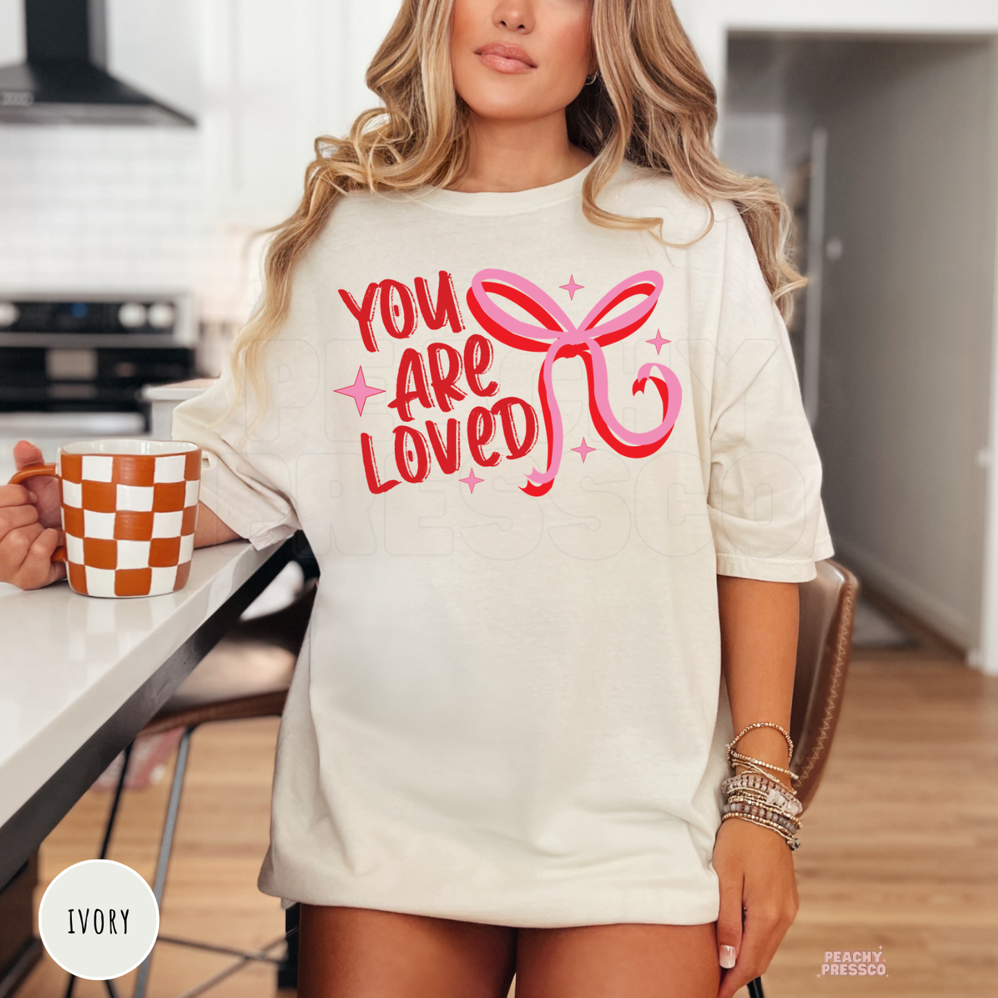 Ivory unisex Valentine's Day t-shirt with a vintage "You Are Loved" quote and pink ribbon bow graphic.