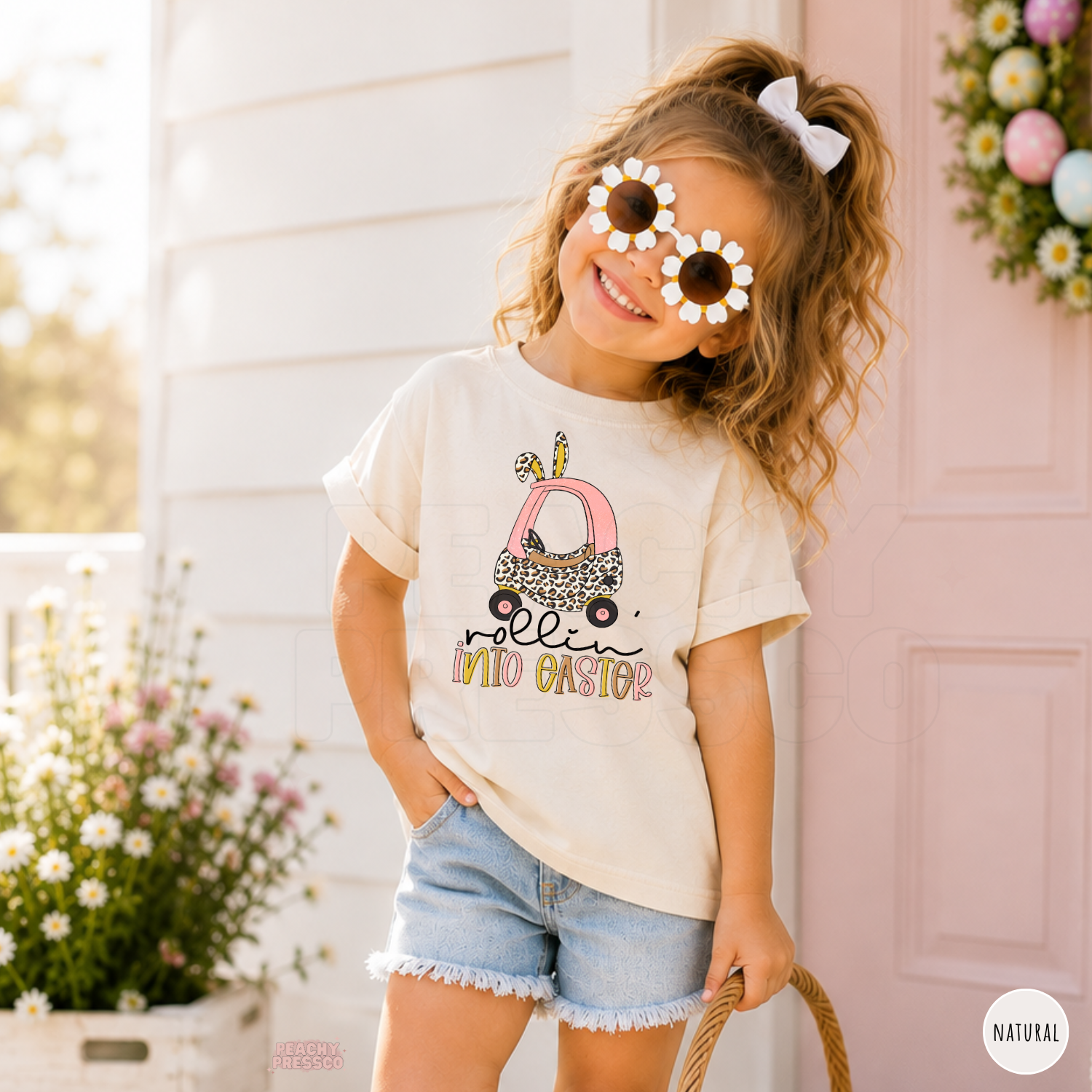 Girl smiling in a natural Rollin Into Easter shirt featuring a pink bunny car with leopard print and Easter design.